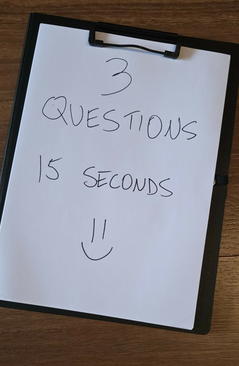 A handwritten sign on a clipboard reading "3 questions, 15 seconds" with a smiley face